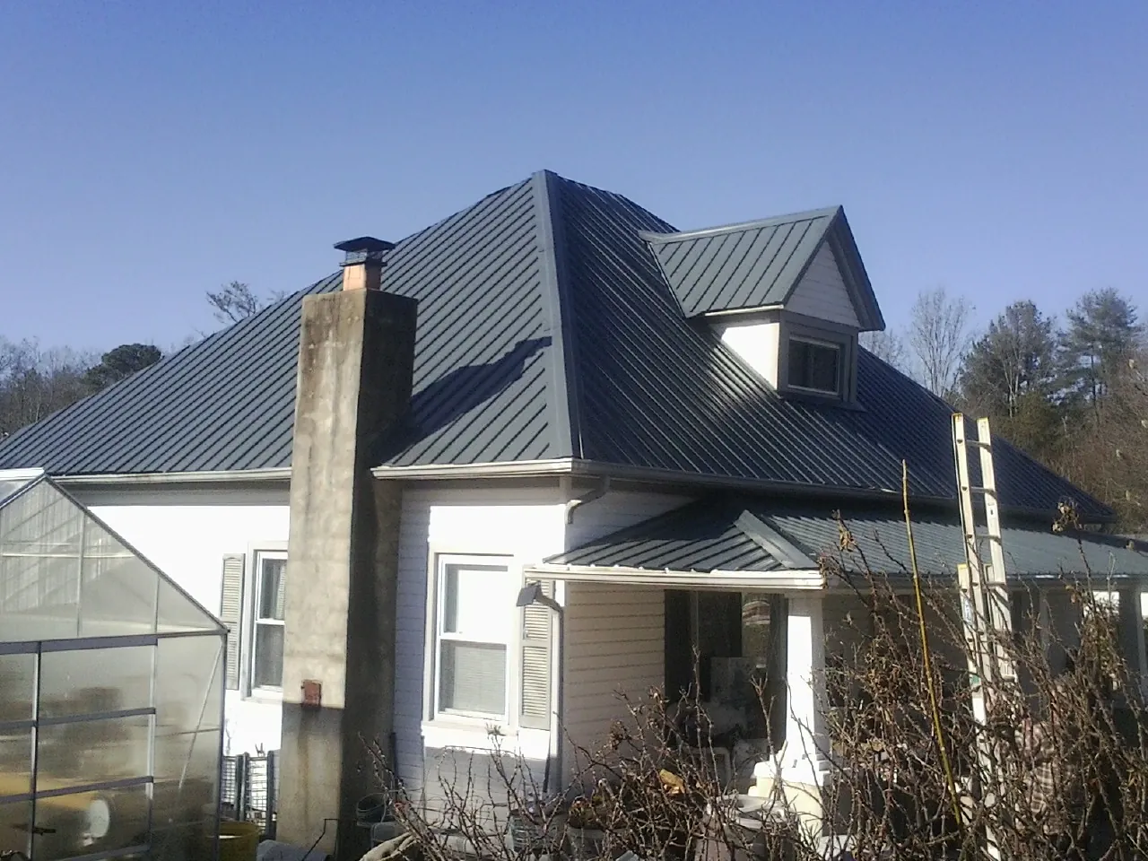 Dark blue standing seam metal roof on a white farmhouse with dormer — Slate & Tile Roof Repair by Roofing Brothers in Dimondale