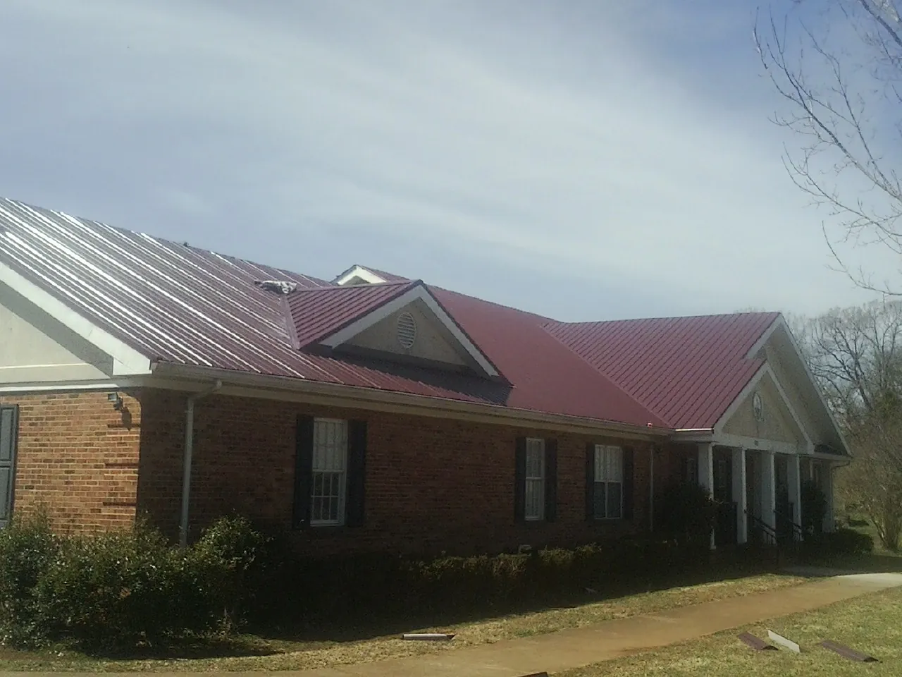 Red metal roof with gabled entries on a long brick building, from a Hail Damage Roof Repair job in Dimondale