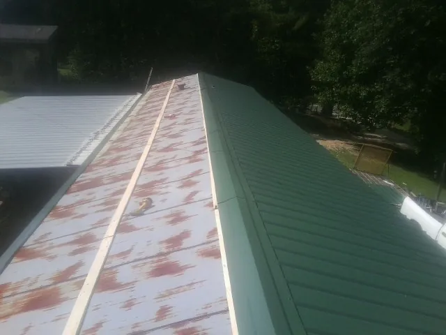 Old rusted panels beside newly installed green metal roofing — Wind Damage Roof Repair by Roofing Brothers in Dimondale