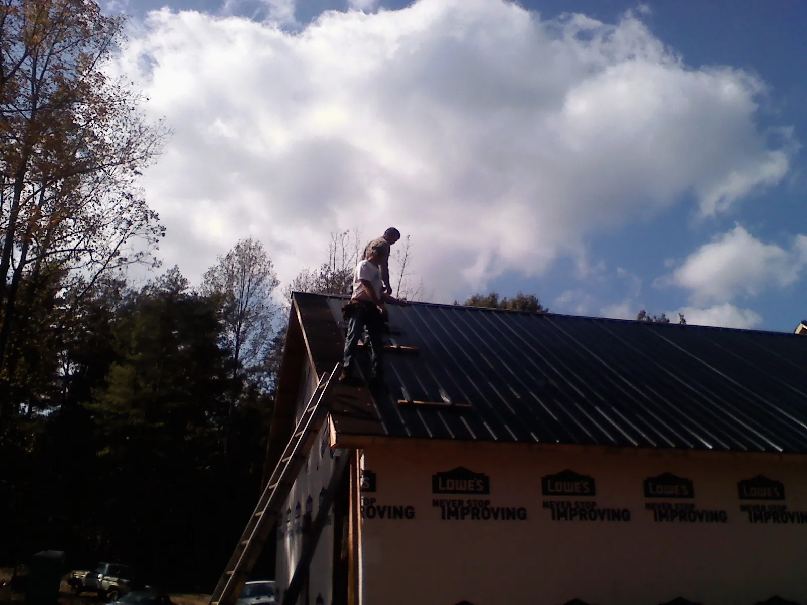 Roofer fastening dark metal panels high against a cloudy sky, from a Roof Inspection job in Dimondale