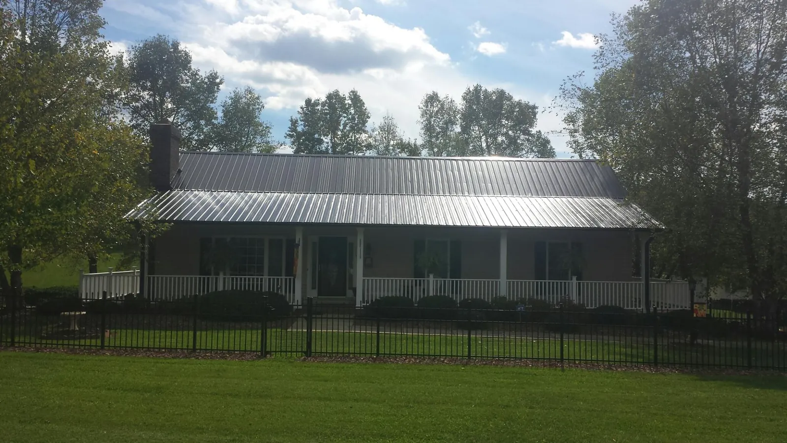 Gray metal roof on a brick ranch with a full width front porch — Gutter Guard Installation work by our crew in Dimondale