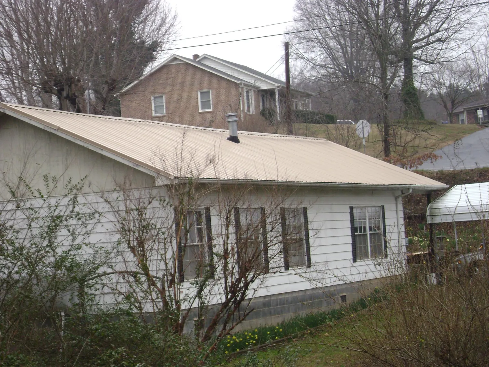 Tan metal roof on a white sided house set into a hillside — Commercial Roofing by Roofing Brothers in Dimondale