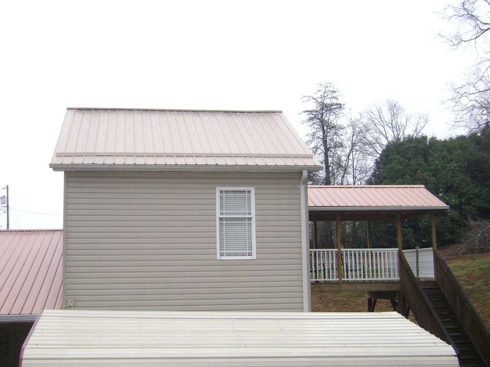 Tan metal roofs on a two story addition and attached porch, from a Roof Replacement job in Dimondale
